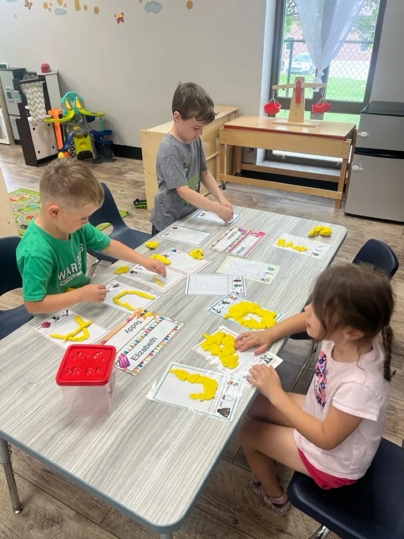 Children shaping letters and numbers with playdough at a classroom table