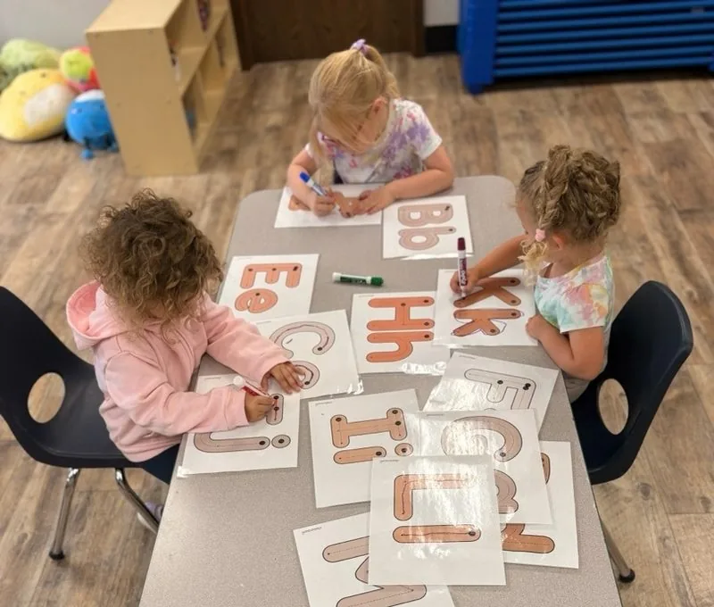 Children tracing letters with dry-erase markers on laminated cards